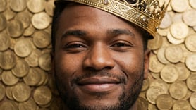 A Nigerian prince wearing a gold crown and surrounded by coins.